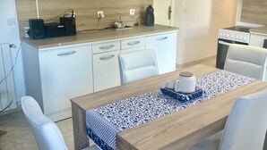 Moderni keittiö, jossa on valkoiset kaapit, puinen työtaso ja ruokailutila, jossa on neljälle katettu ruokapöytä.