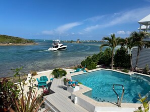 A pool area with lounge chairs, a boat on the water, and a view of the ocean.