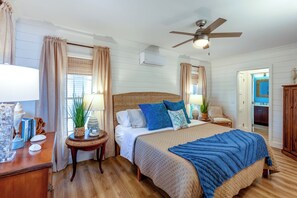 A bedroom with a large bed, a ceiling fan, and a view of the bathroom.