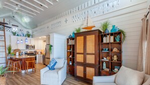 A spacious living room with a large wooden cabinet, two white armchairs, and a kitchen area visible in the background. - Saltwater Sanctuary-Secret garden in a tropical paradise (Hope Town)