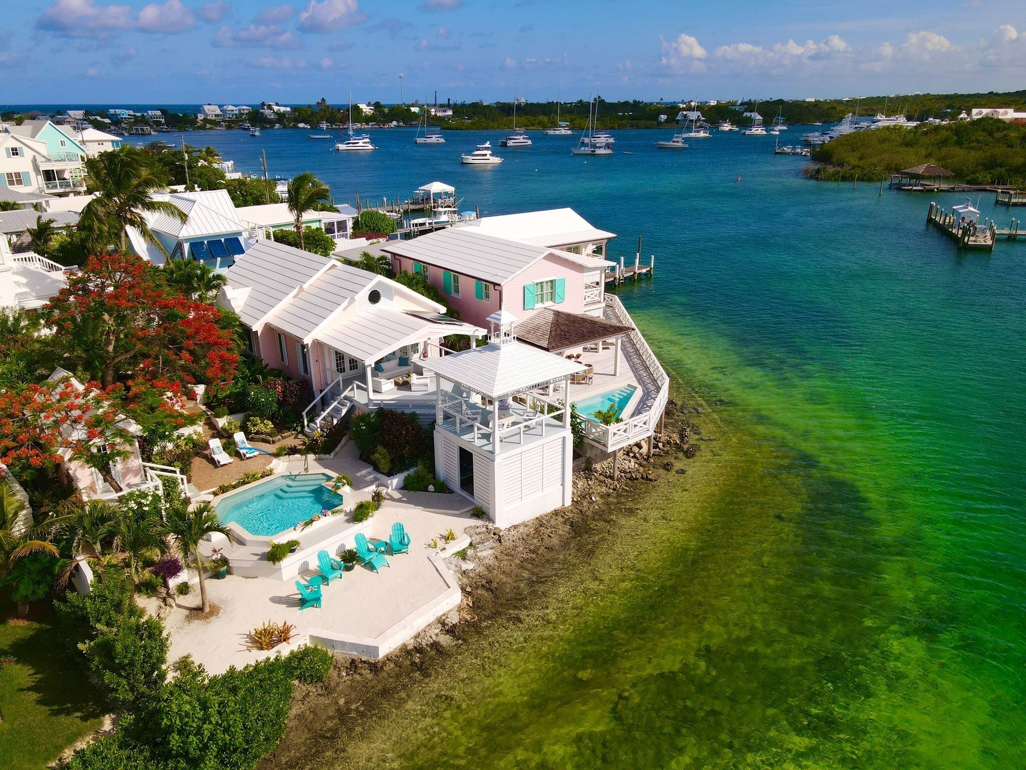 A coastal property with a swimming pool, multiple decks, and a view of the marina with boats.