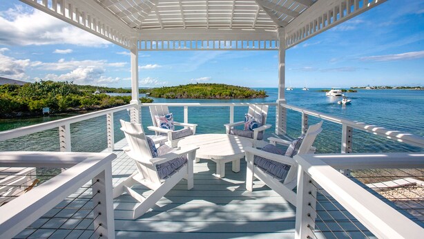 A covered outdoor deck with white railings and lounge chairs, overlooking a clear blue sea with boats and a small island in the distance. - Saltwater Sanctuary-Secret garden in a tropical paradise (Hope Town)