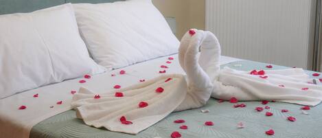 Una cama con almohadas blancas, una toalla con forma de cisne y pétalos de rosa esparcidos.