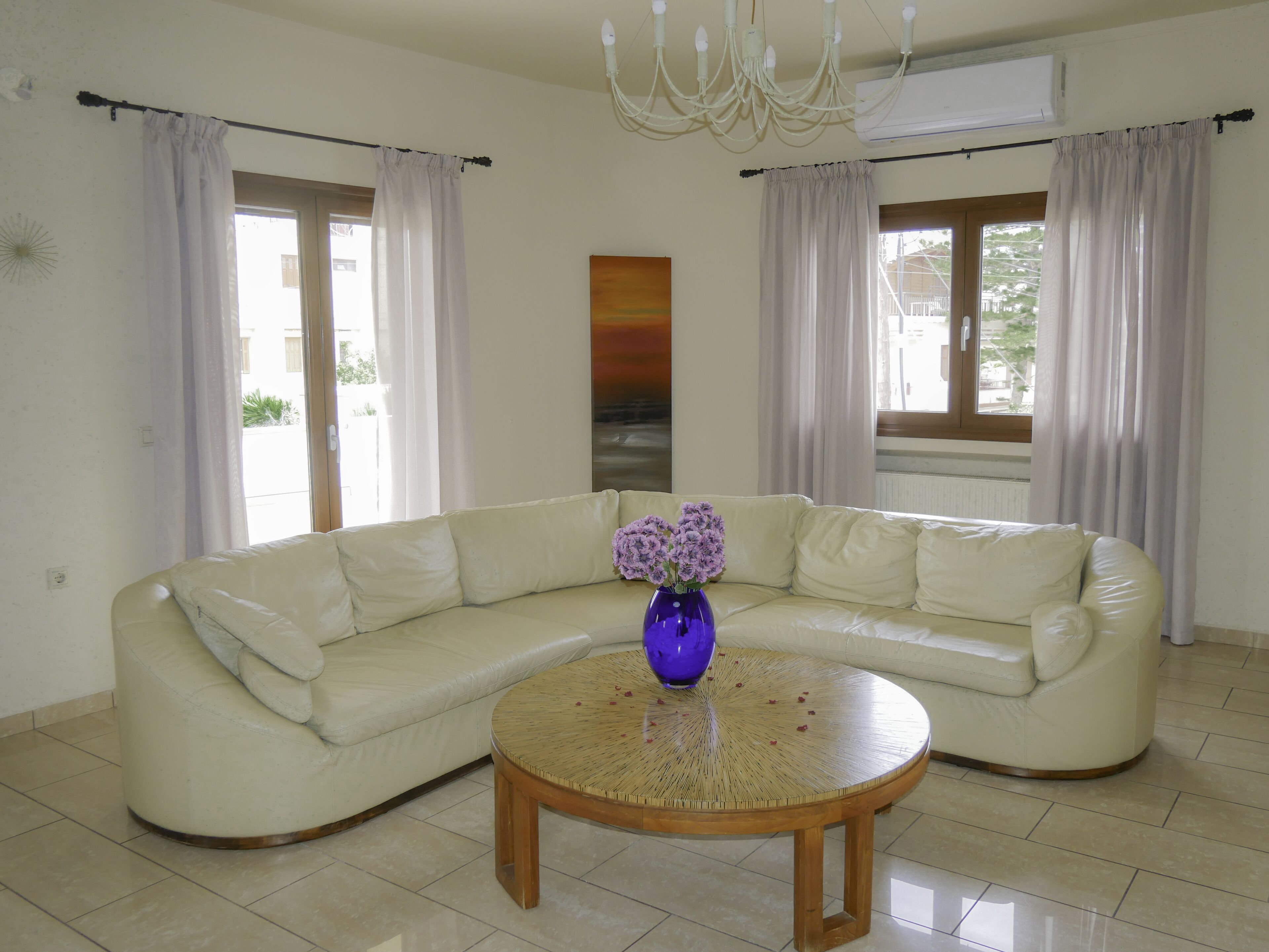 A living room with a beige sectional sofa, a round wooden coffee table, and a purple vase with flowers.