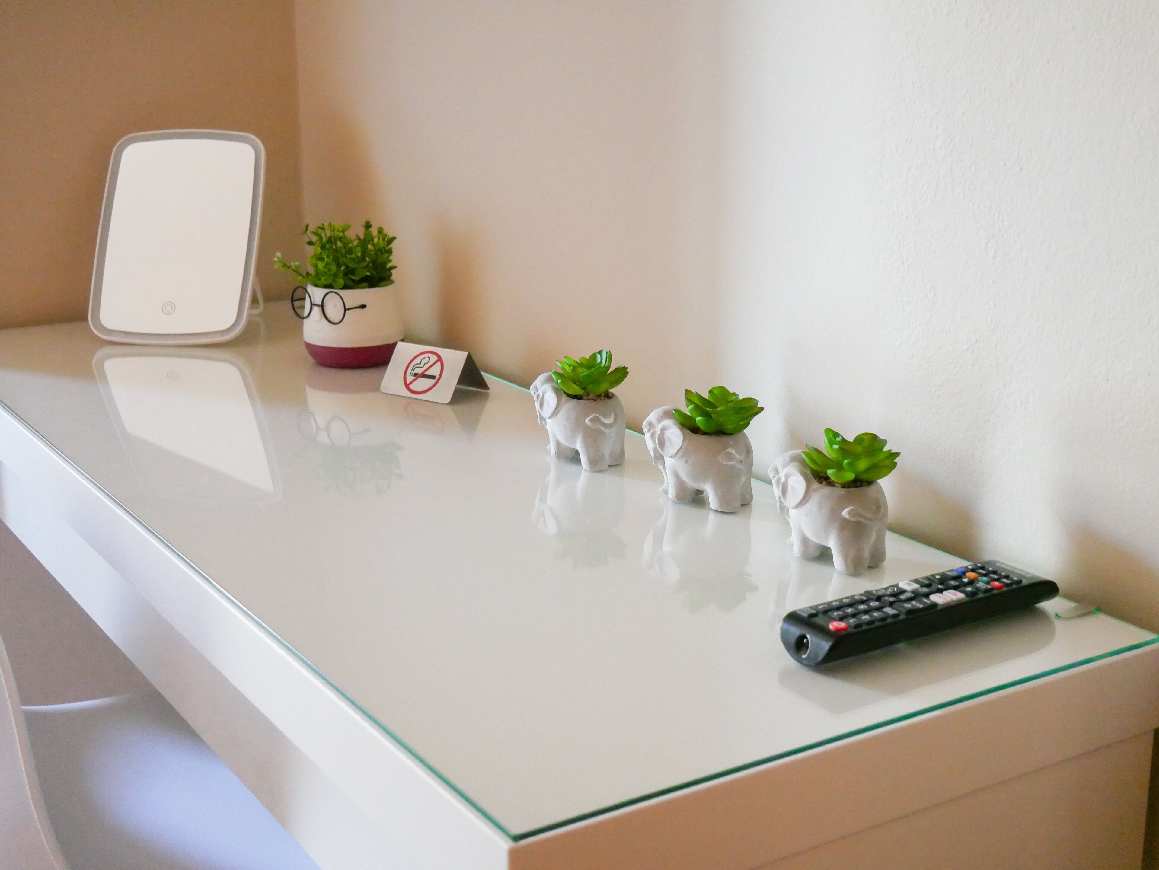 A white table with a remote control, three small elephant-shaped planters with succulents, a no-smoking sign, and a white device with a red button.