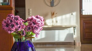 Une pièce avec un vase bleu contenant des fleurs roses, une horloge au mur et un radiateur.