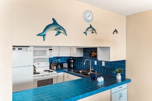 Una cocina con azulejos azules, armarios blancos, microondas, estufa, lavabo y decoración con motivos de delfines.