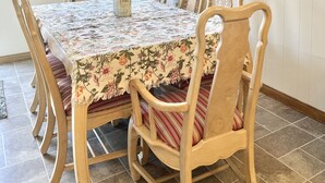 A dining room with a floral tablecloth, wooden chairs, and framed botanical prints on the wall. - Lee’s Garden House (Oskaloosa)