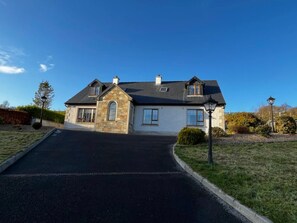 A two-story house with a stone facade, a black roof, and a driveway leading to the entrance. - *Walk to Beach | Spacious & Clean | Ocean Views* (DL)