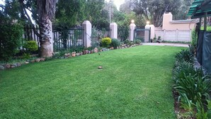 A well-maintained lawn with a stone border, a metal fence, and a variety of plants.