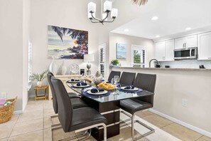 Une cuisine moderne avec des meubles blancs, un four à micro-ondes en acier inoxydable et un coin repas comprenant une table en verre et des chaises noires.