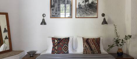 A neatly arranged hotel room with a bed, two wall-mounted lamps, a small table with a bowl, and two framed pictures on the wall.