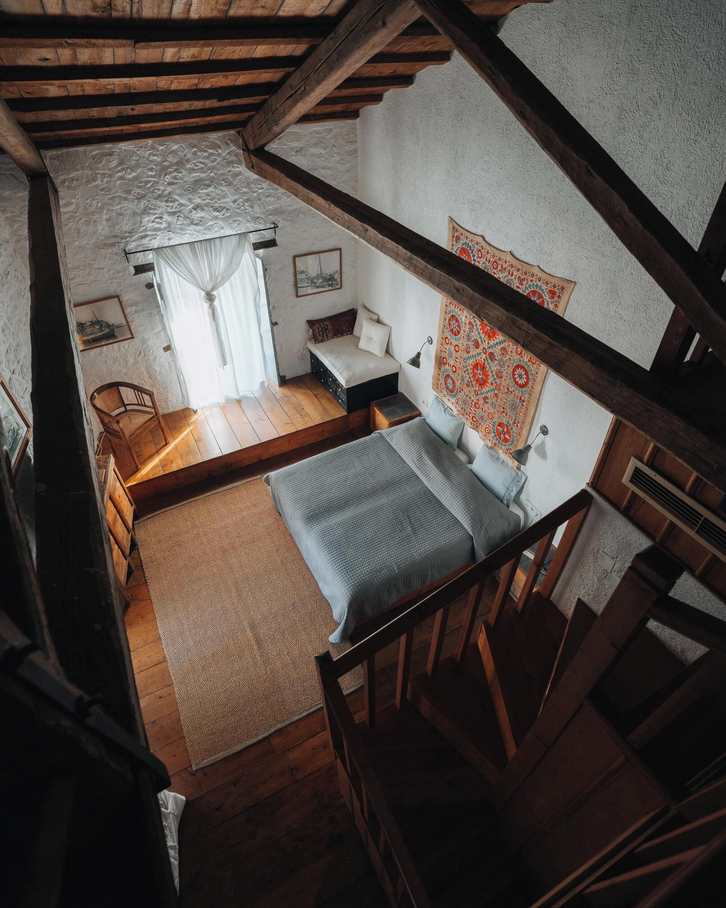 A rustic bedroom with a loft bed, a small bedside table, a chair, and a patterned tapestry.