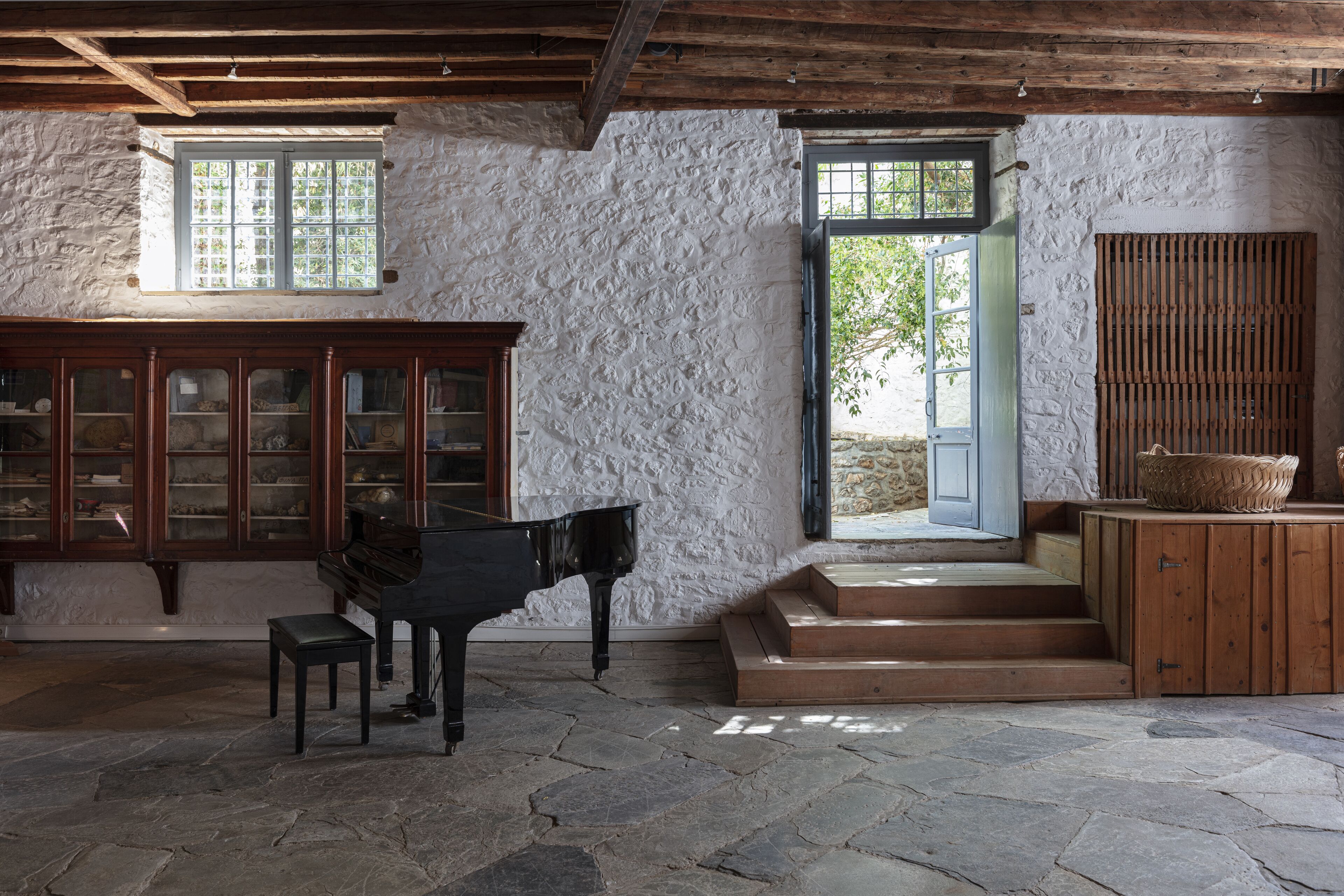 A room with a piano, a wooden cabinet, and a stone floor.