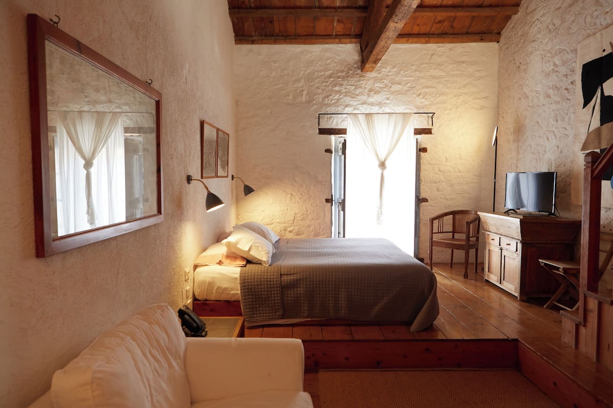 Une chambre confortable avec un lit, un bureau et une chaise. Il y a une fenêtre avec des rideaux et un miroir au mur.