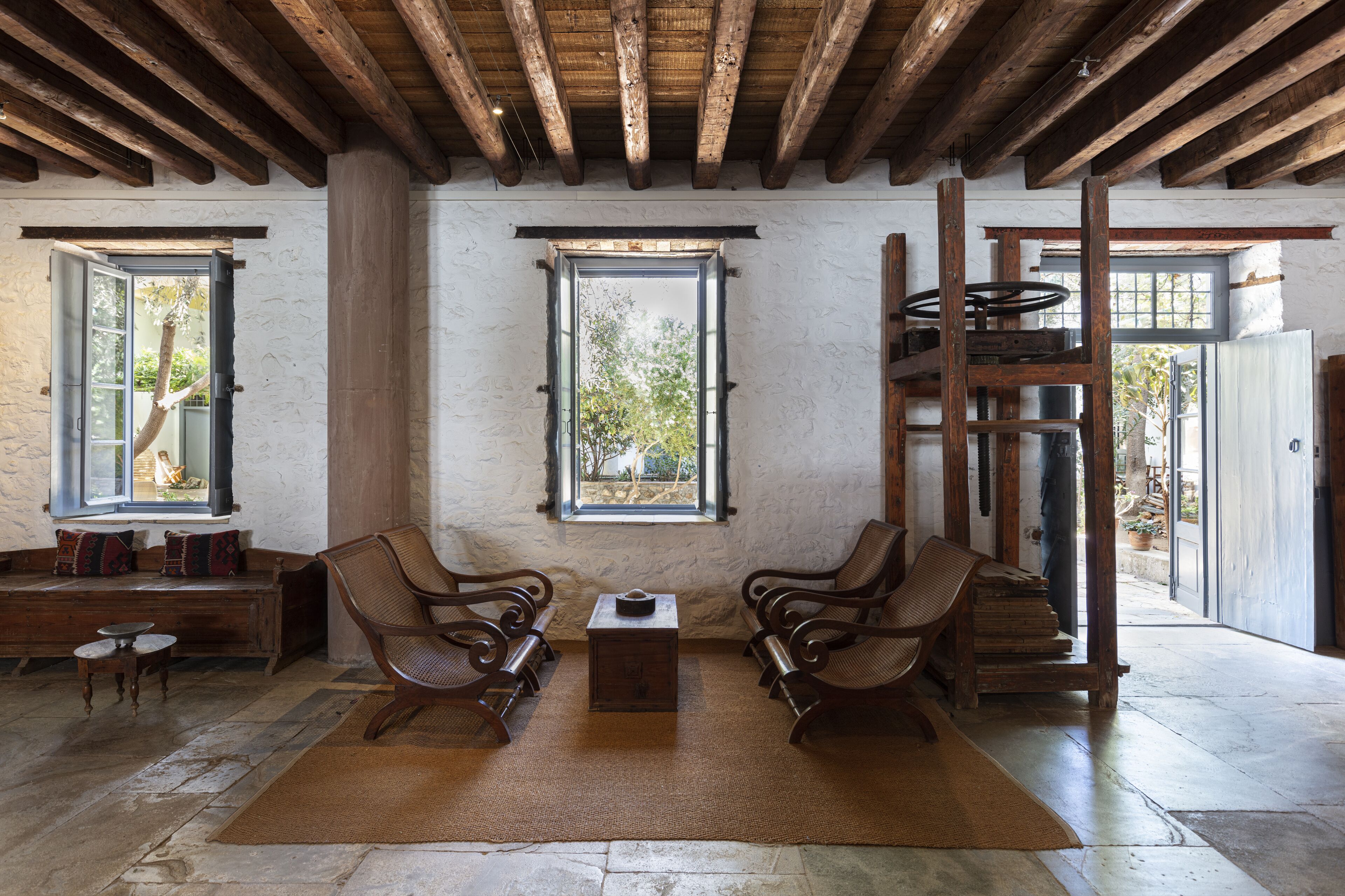 A rustic interior with wooden beams, a stone floor, and a bench with cushions.