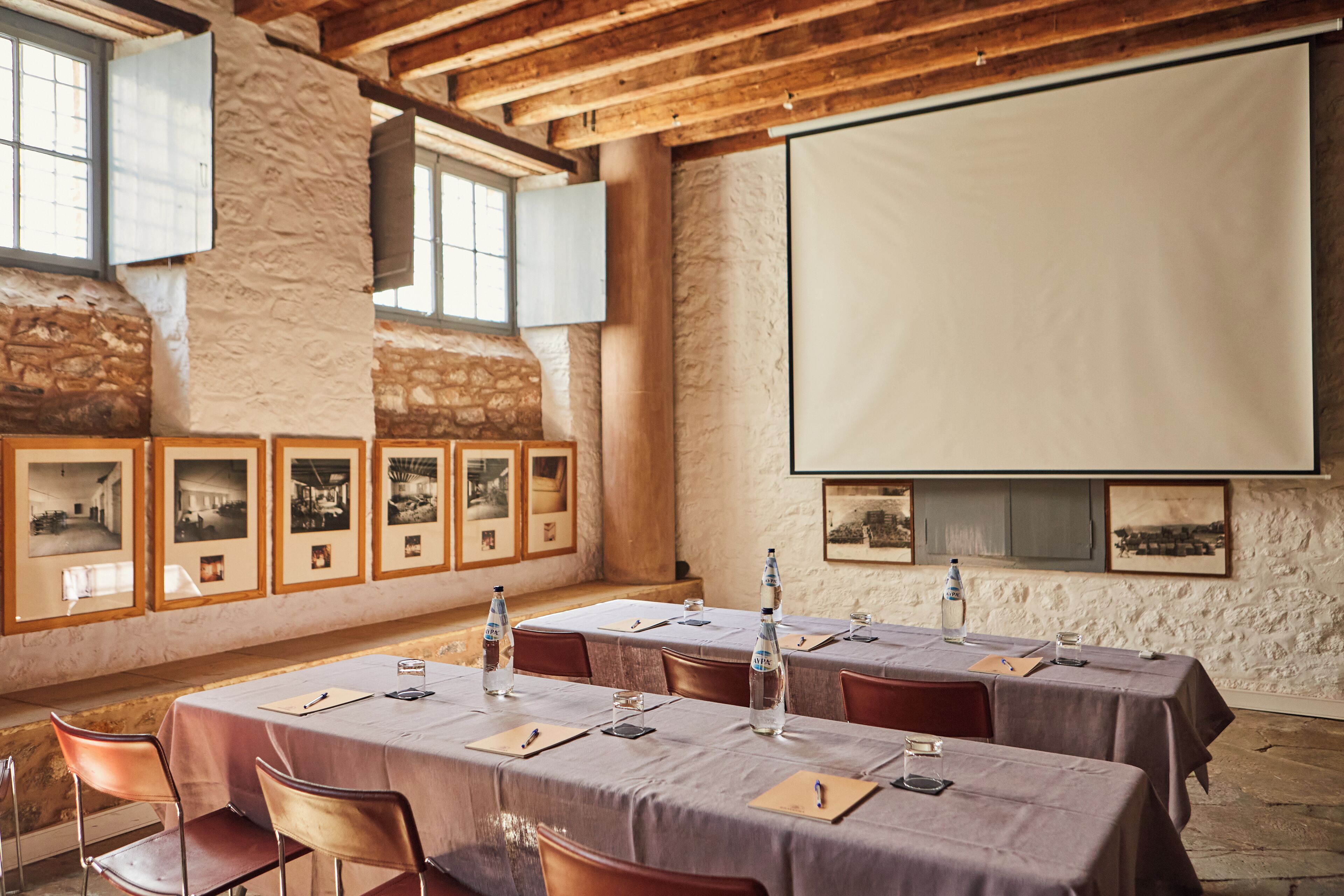 A conference room with tables set for a meeting, framed pictures on the wall, and a projector screen.