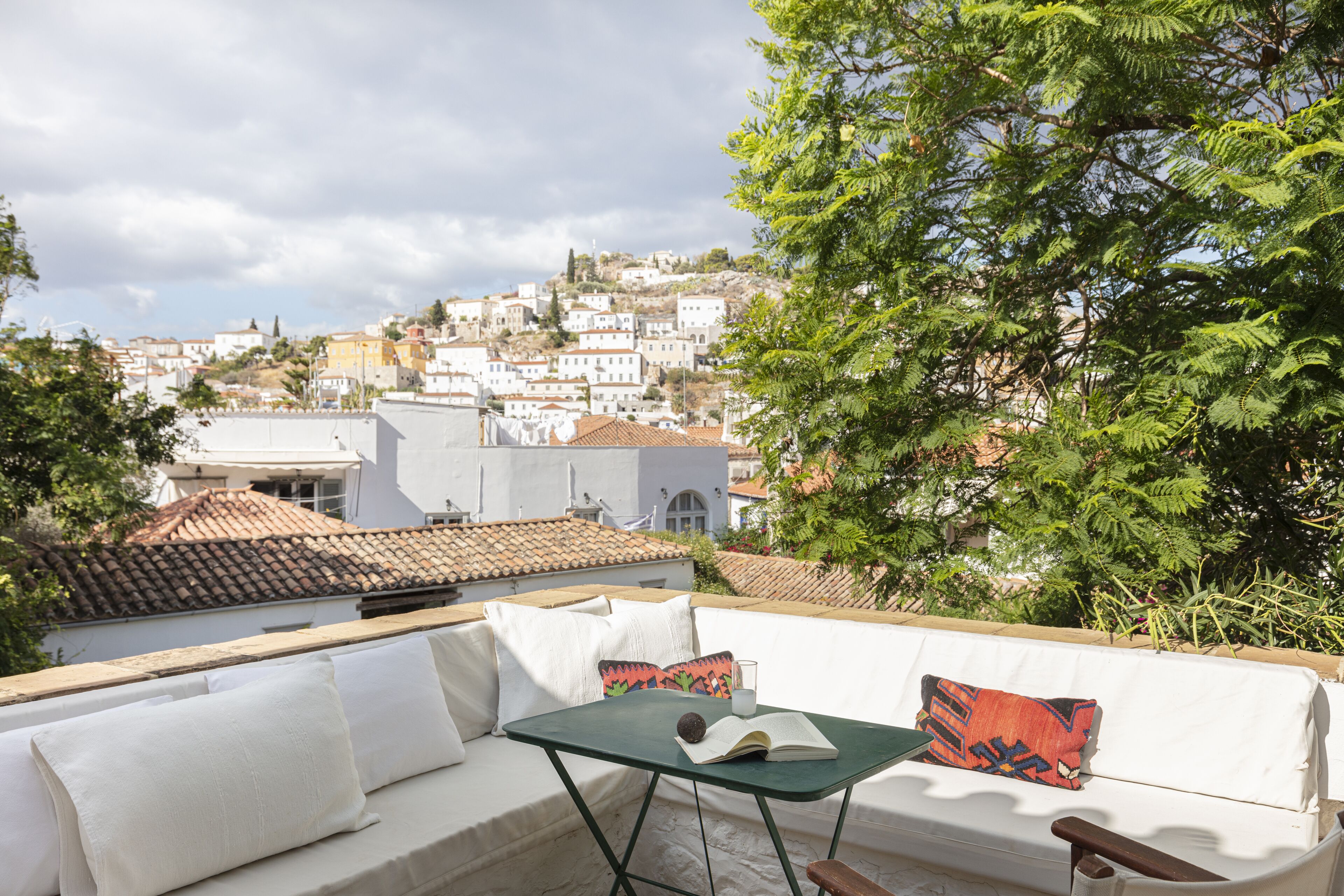Una terraza en la azotea con un sofá blanco, una mesita y vistas a un pueblo en la colina.