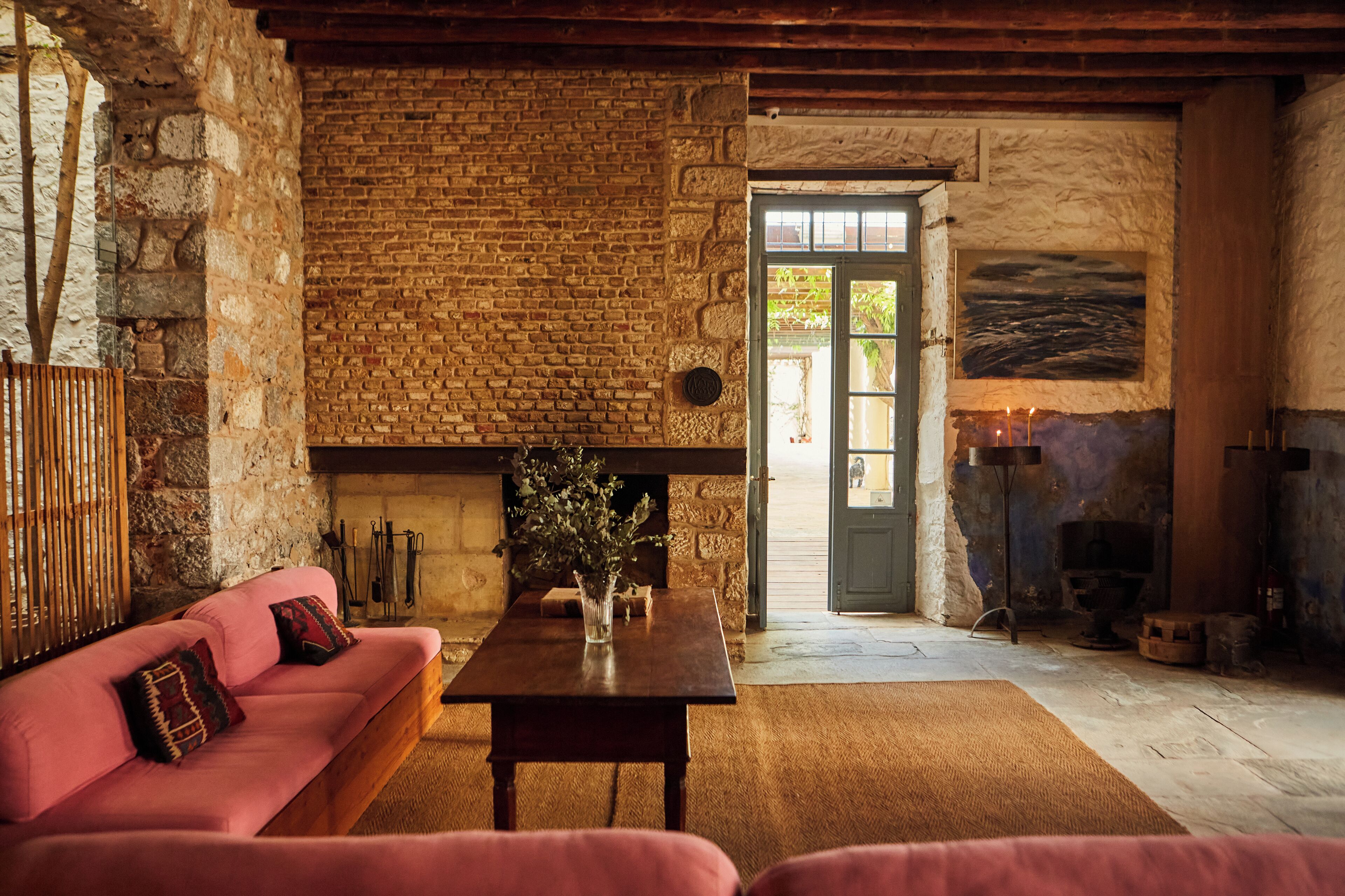 Un interior rústico con una pared de piedra, una mesa de madera, un sofá rosa y una chimenea.