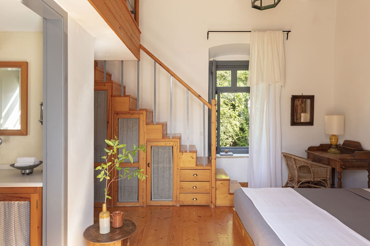 Une chambre avec un escalier en bois, un lit, un bureau et une fenêtre avec des rideaux.