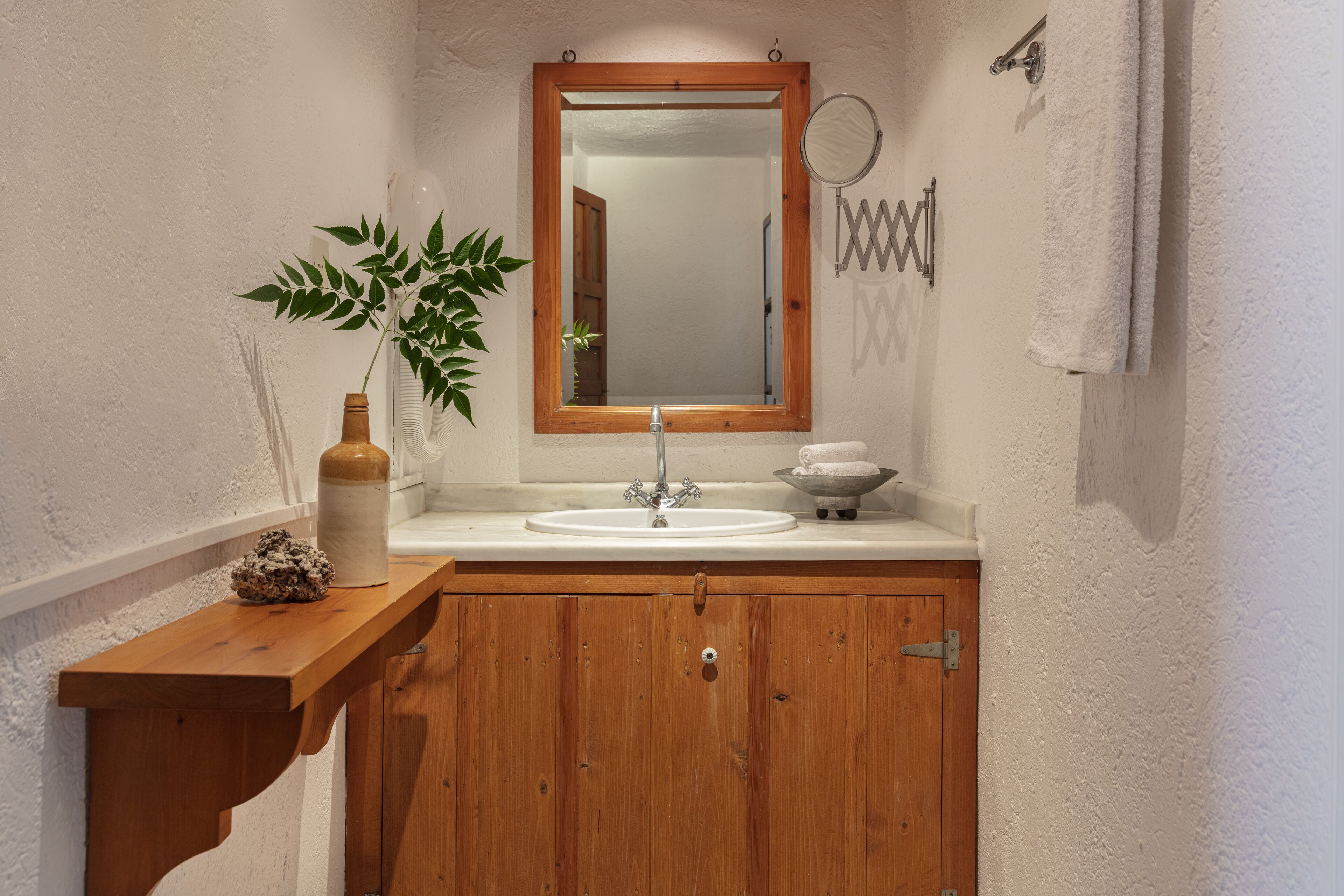 A bathroom with a wooden vanity, a white sink, a mirror, and a plant.