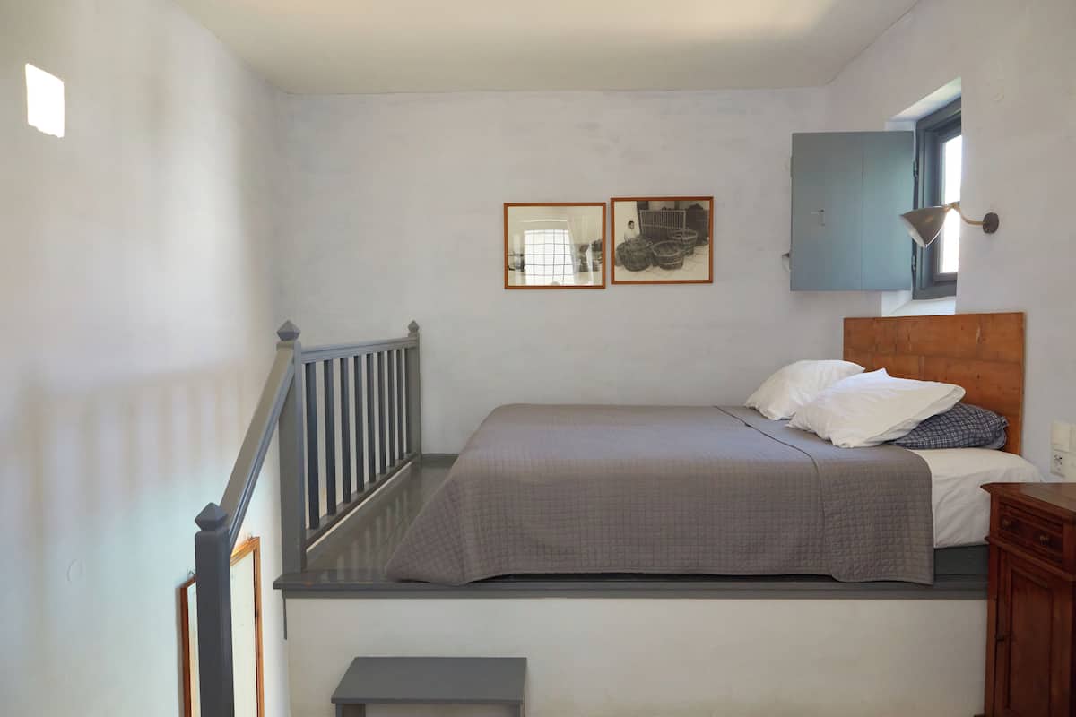 Une chambre à coucher comprenant un lit, une tête de lit en bois, une table de chevet, une commode, une fenêtre avec vue et un escalier.