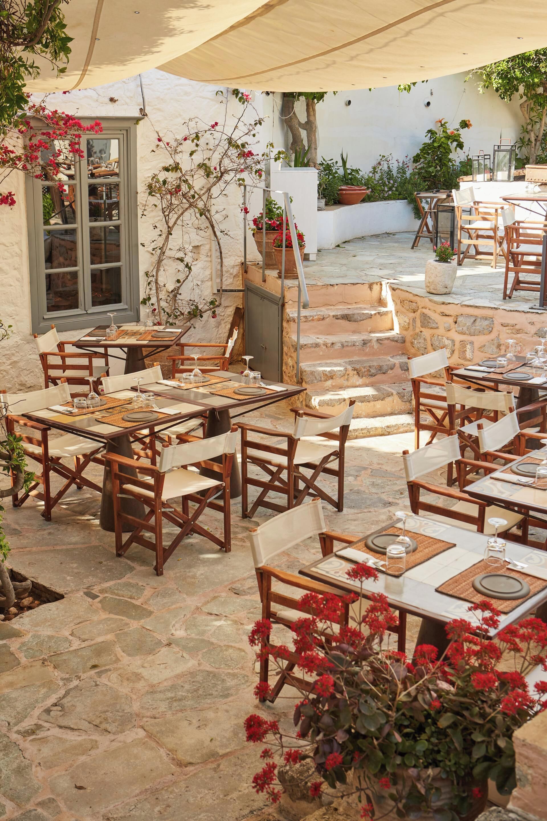 Un espace extérieur aménagé en terrasse, avec un sol en pierre, des tables et des chaises en bois, et des plantes en pot.