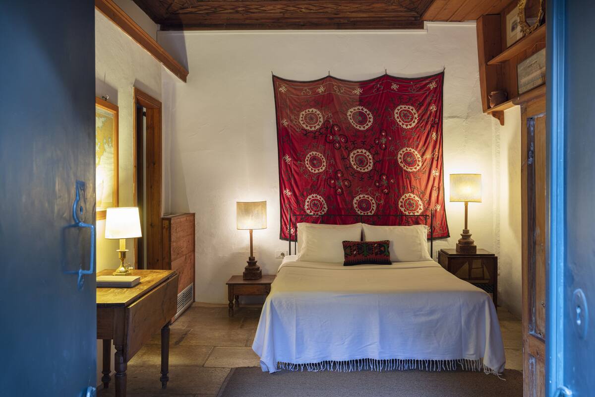 Une chambre à coucher avec un grand lit, deux tables de chevet avec des lampes, une tapisserie rouge au mur et une tête de lit en bois.