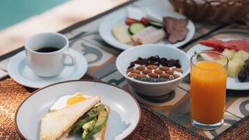 A breakfast setting with a poolside table featuring plates of food, a glass of orange juice, and a cup of coffee.