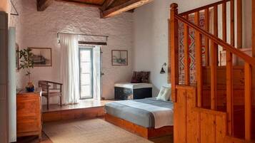 A rustic bedroom with a wooden bed, a desk, and a staircase.