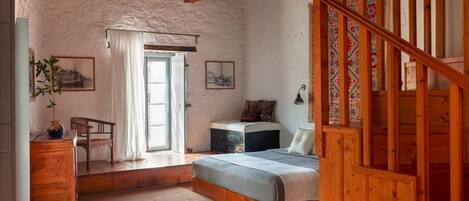 A rustic bedroom with a wooden bed, a desk, and a staircase.