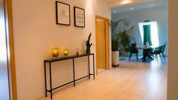 A modern hotel lobby with a wooden console table, framed artwork, and a dining area with chairs and a table.