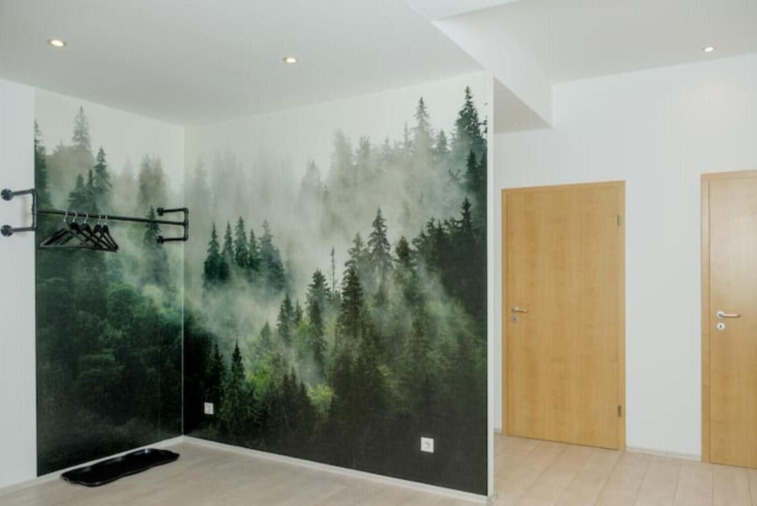 A room with a large wall mural of a forest scene, a wooden door, and a black mat on the floor.