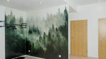A room with a large wall mural of a forest scene, a wooden door, and a black mat on the floor.