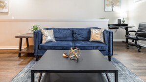 A modern living room with a dark blue sofa, a black coffee table, and a small plant on a side table. - Gym, Fast WiFi, King Bed, Free Parking (Huntsville)
