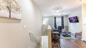 A modern living room with a flat-screen TV, a dining area with a table and chairs, and a staircase leading to another level. - Gym, Fast WiFi, King Bed, Free Parking (Huntsville)