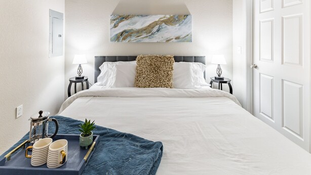 A neatly arranged hotel room with a large bed, two bedside tables with lamps, a coffee maker, and a tray with mugs and a plant. - Gym, Fast WiFi, King Bed, Free Parking (Huntsville)