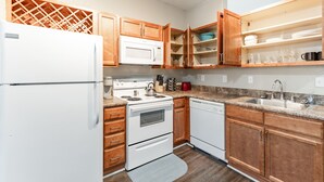A compact kitchen with wooden cabinets, a white refrigerator, a microwave, a stove, and a dishwasher. - Gym, Fast WiFi, King Bed, Free Parking (Huntsville)