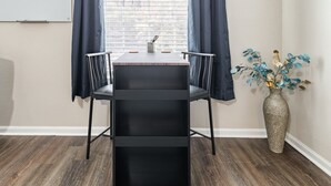 A small, modern room with a black desk and chair, a whiteboard, and a window with blinds. - Gym, Fast WiFi, King Bed, Free Parking (Huntsville)