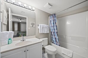 A bathroom with a white sink, mirror, and toilet, a shower curtain, and a towel rack.