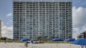 Un hôtel de grande hauteur doté de nombreux balcons, une plage de sable en premier plan et un ciel dégagé.