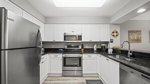 Une cuisine moderne dotée d’appareils électroménagers en acier inoxydable, de meubles blancs et d’un plan de travail noir.