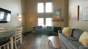 Una sala de estar con sofá, una mesa de comedor con sillas, un televisor y obras de arte en las paredes.