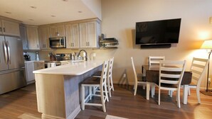 Una cocina moderna con una isla central, armarios blancos, electrodomésticos de acero inoxidable y un televisor de pantalla plana montado en la pared.