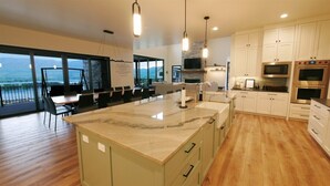 A modern kitchen with a large island, built-in appliances, and a view of the outdoors. - The Pickleball Gathering Place (Huntsville)