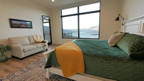A bedroom with a large window, a bed, a sofa, and a view of a body of water.
