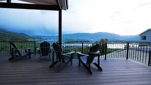 A wooden deck with Adirondack chairs and tables, overlooking a lake and mountains. - The Pickleball Gathering Place (Huntsville)
