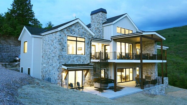 A two-story house with a stone facade, large windows, and a covered outdoor seating area. - The Pickleball Gathering Place (Huntsville)