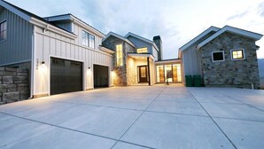 A modern multi-story house with a garage, stone exterior, and a spacious paved driveway. - The Pickleball Gathering Place (Huntsville)