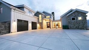 A modern multi-story house with a garage, stone exterior, and a spacious paved driveway.